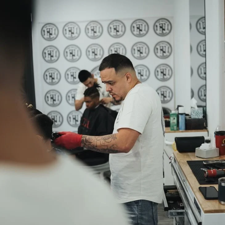 Barber cutting a client's hair in a barbershop with a patterned wall background.