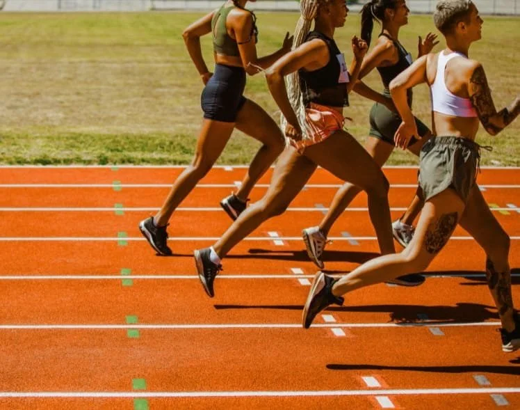 A group of female runners competing in a race on an outdoor track.