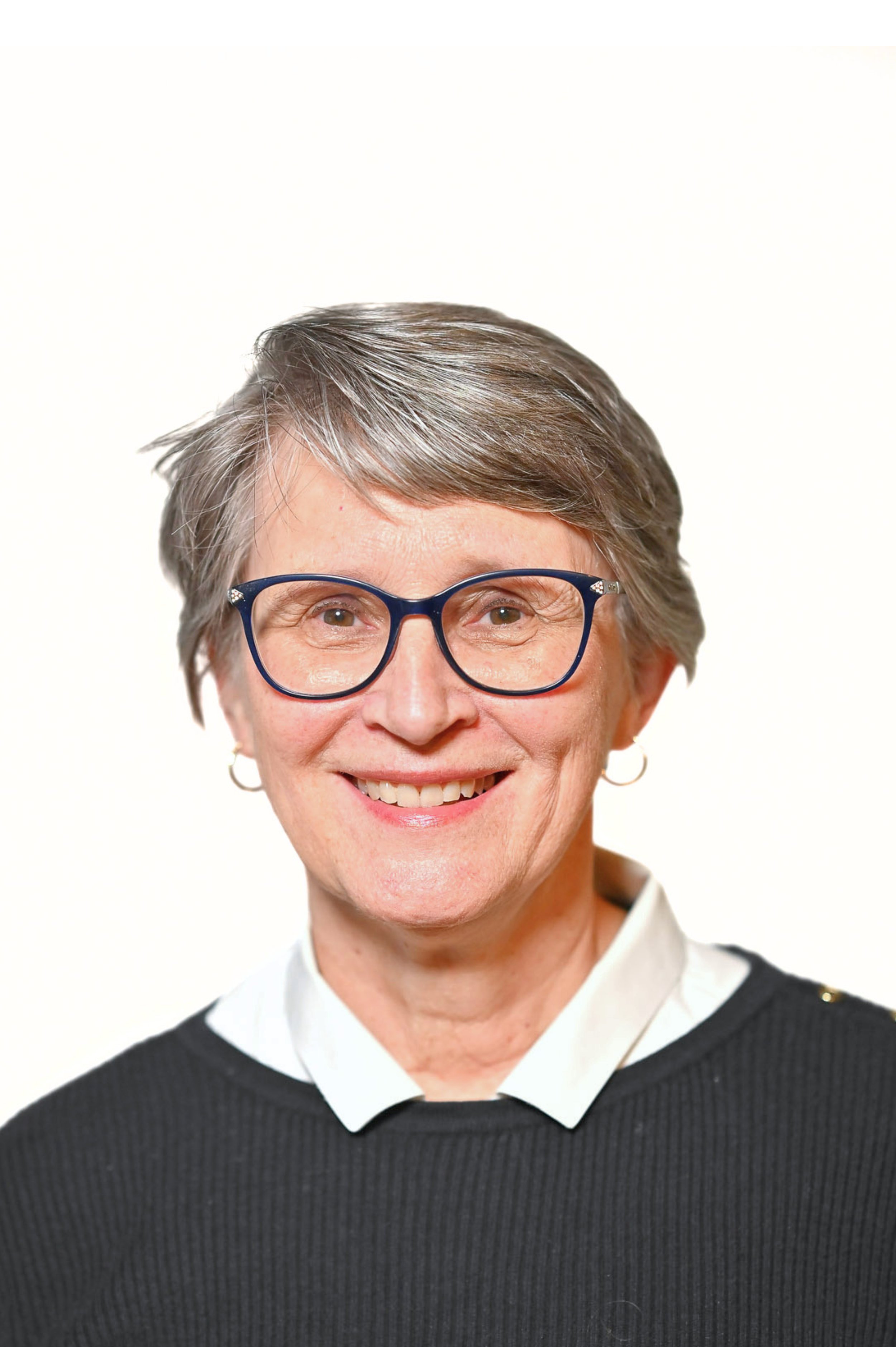 Smiling person wearing glasses and a black sweater with a white shirt underneath, posing against a plain background.