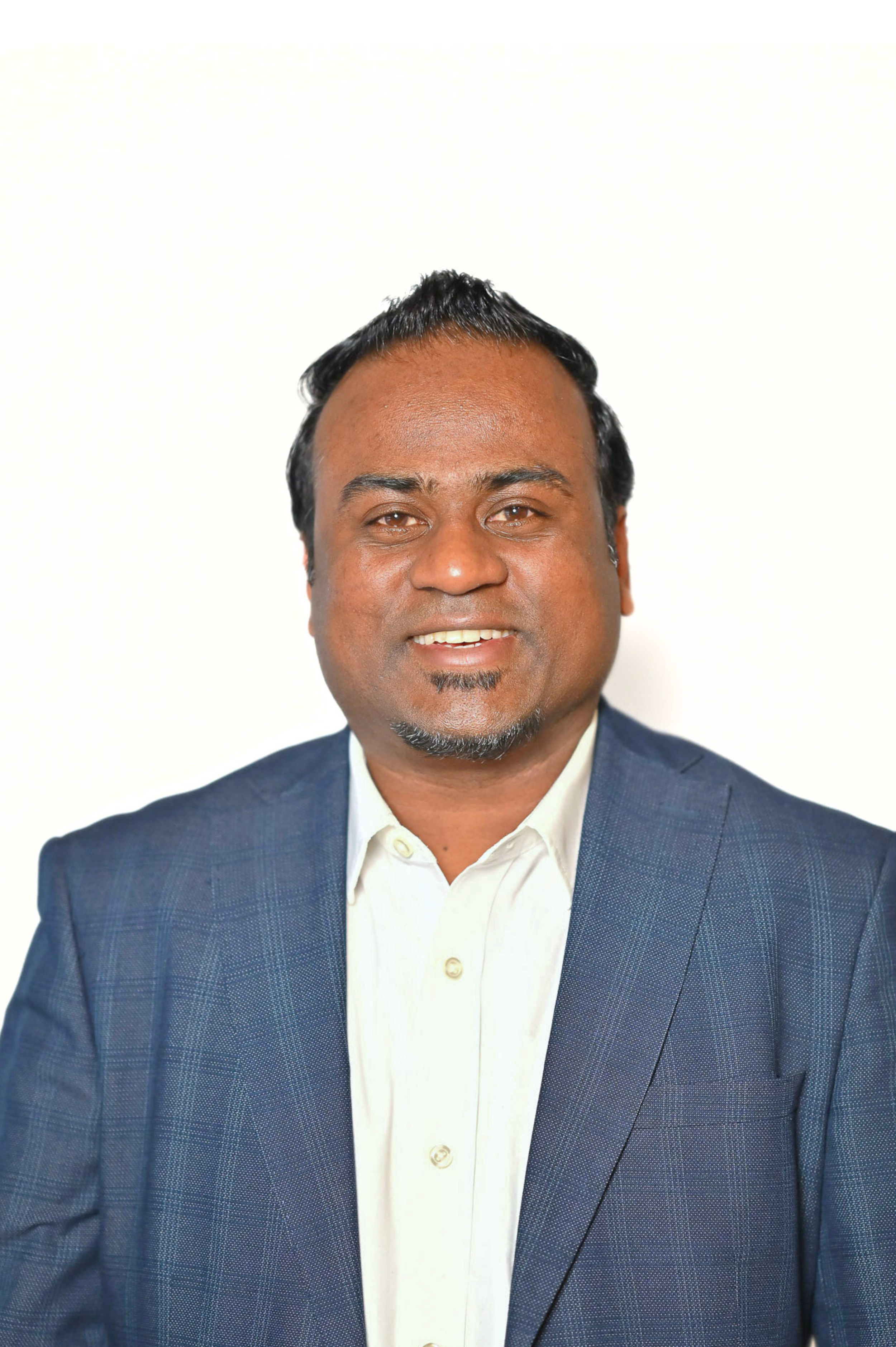 Man smiling in a blue suit jacket and white shirt against a plain background.