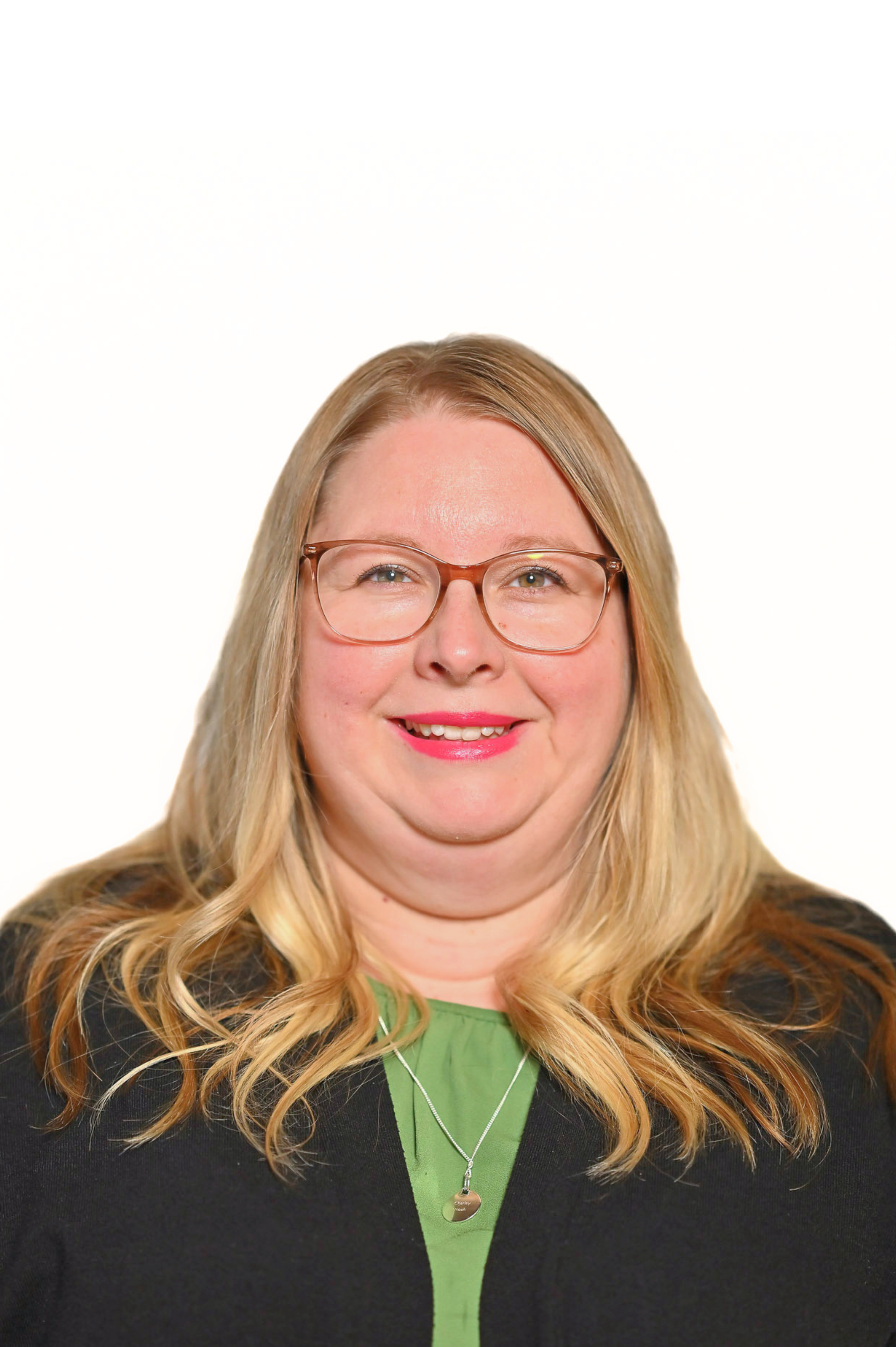 Person with long blond hair, glasses, and wearing a green top and black cardigan