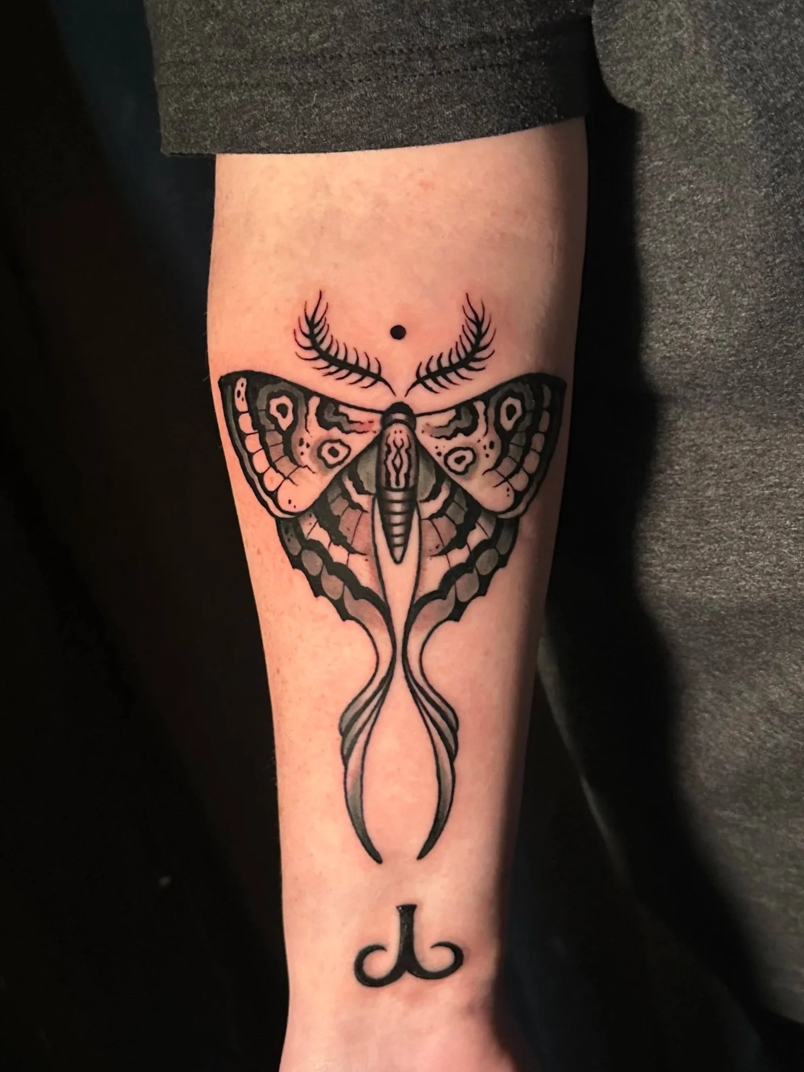Tattoo of a neo traditional moth with detailed black and pink wings, antennae, and a small black dot above its head on a person's arm. 