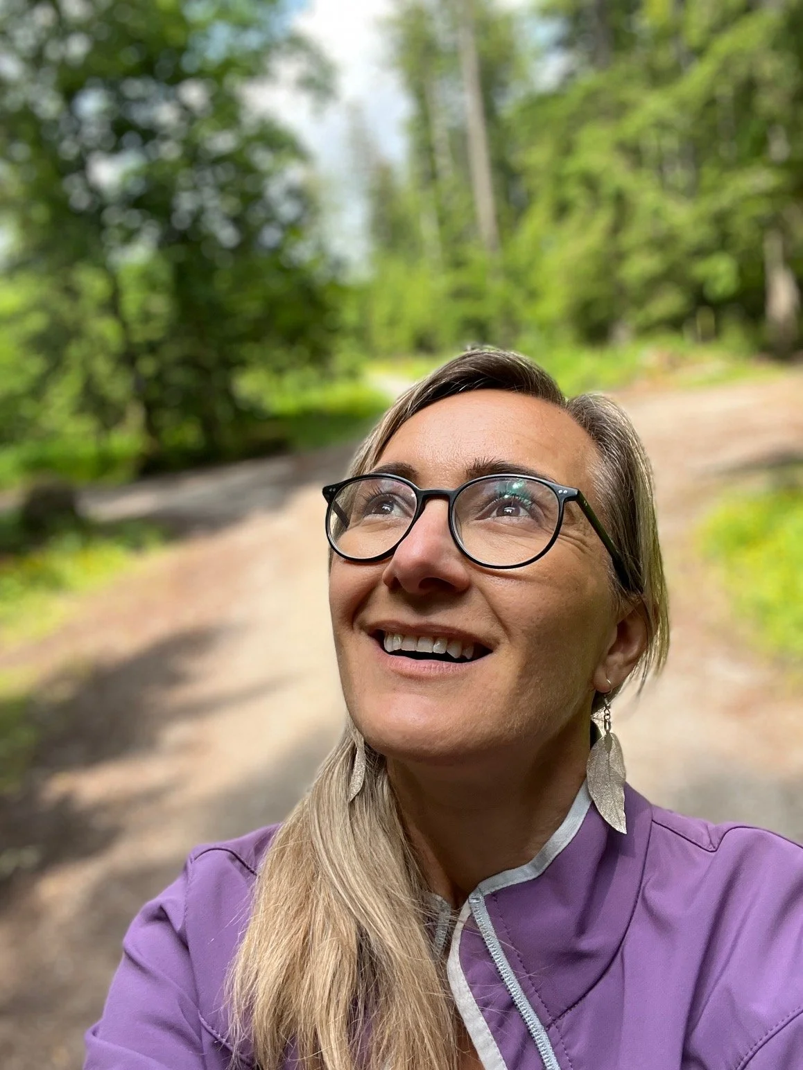 Lächeln, glückliche Frau nach oben in den Himmel guckend. Im Hintergrund einen Waldweg zusehen.