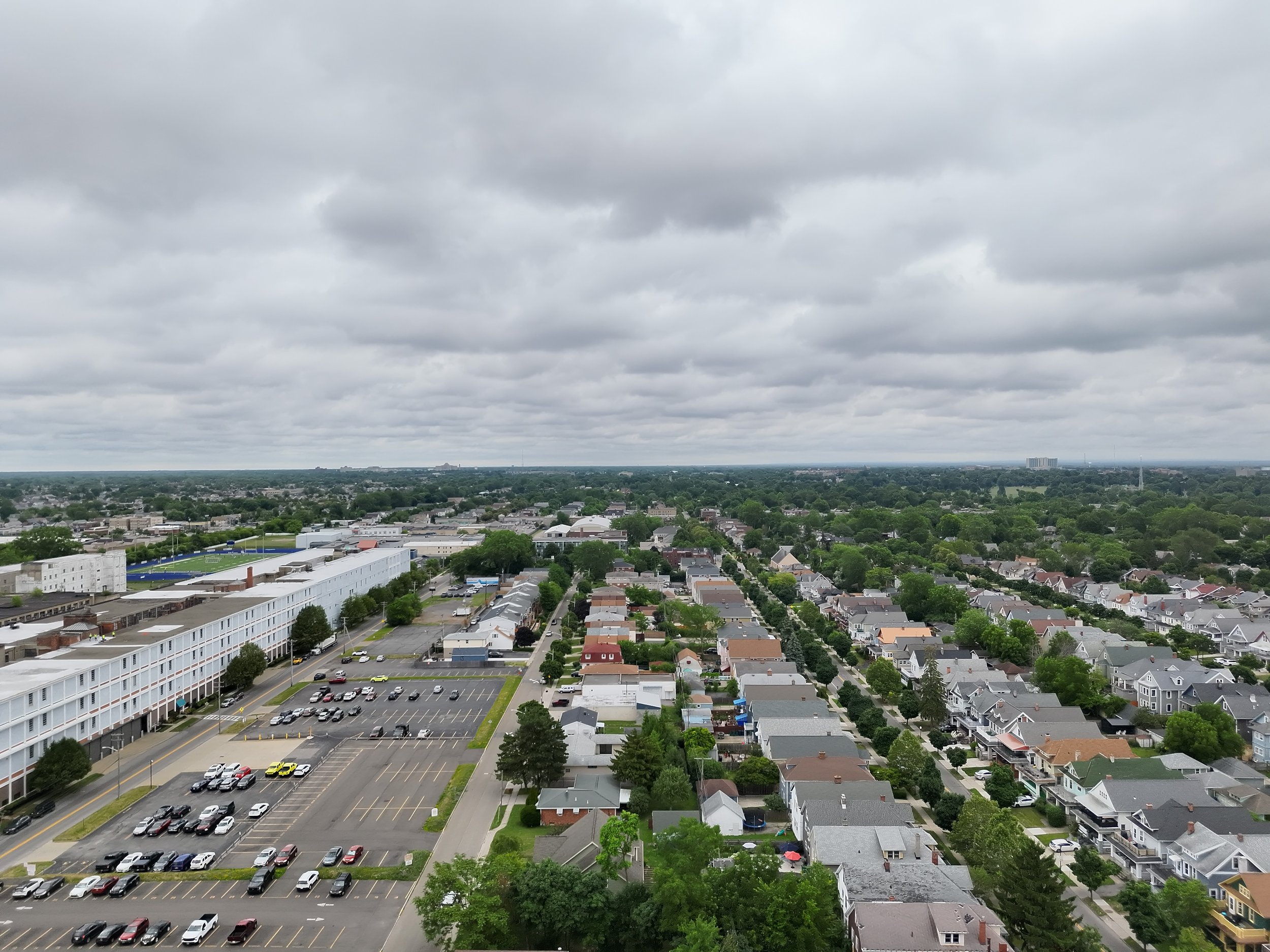 Aerial view of a suburban neighborhood with rows of houses, streets, and a large parking lot on an overcast day.