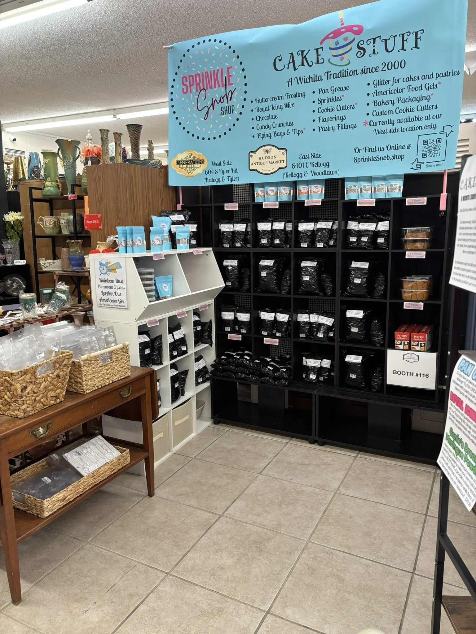 A display of various cake supplies including frosting, sprinkles, and cookie cutters at a store, with a large blue sign overhead advertising the products.