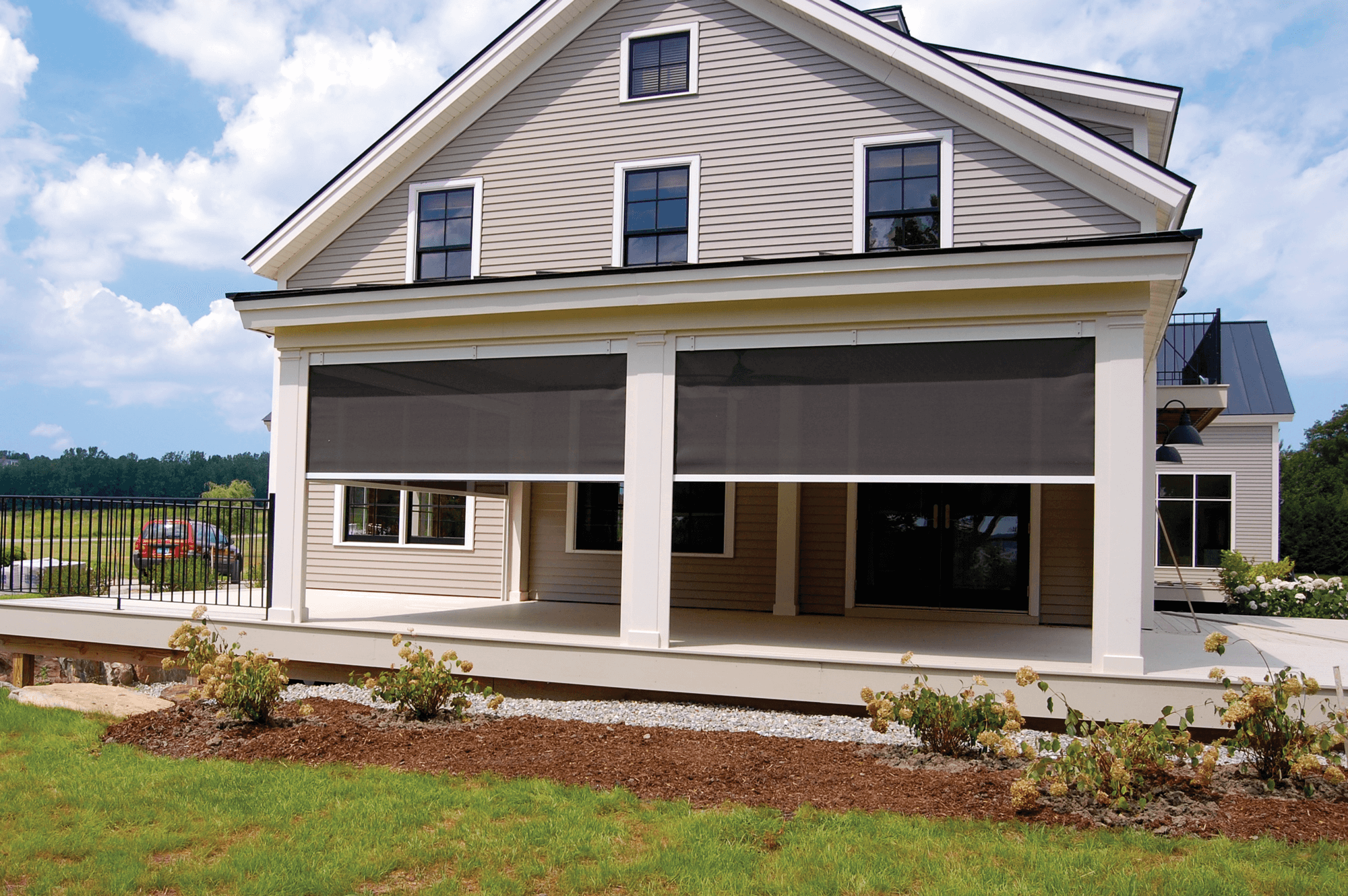 Back view of a modern house with a screened-in porch, lawn, and landscaping, under a partly cloudy sky.