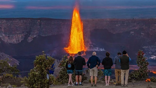 Group of seven people watching erupting volcano with lava coming out.