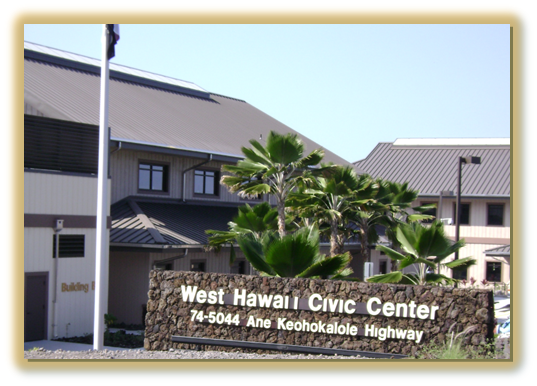 Sign for West Hawaii Civic Center in front of a building with palm trees and a flagpole in Hawaii.
