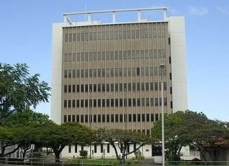 A tall office building with several floors, surrounded by trees and a clear blue sky.
