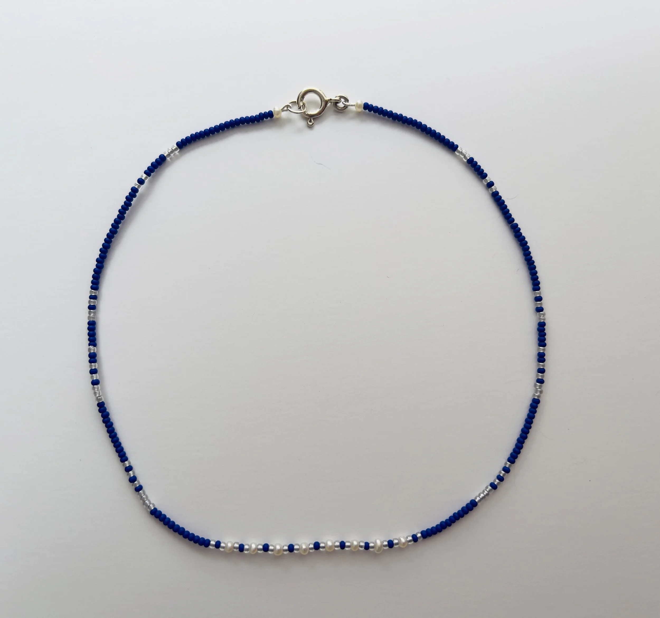 Beaded necklace with blue, white, and silver beads and a silver clasp, displayed against a white background.