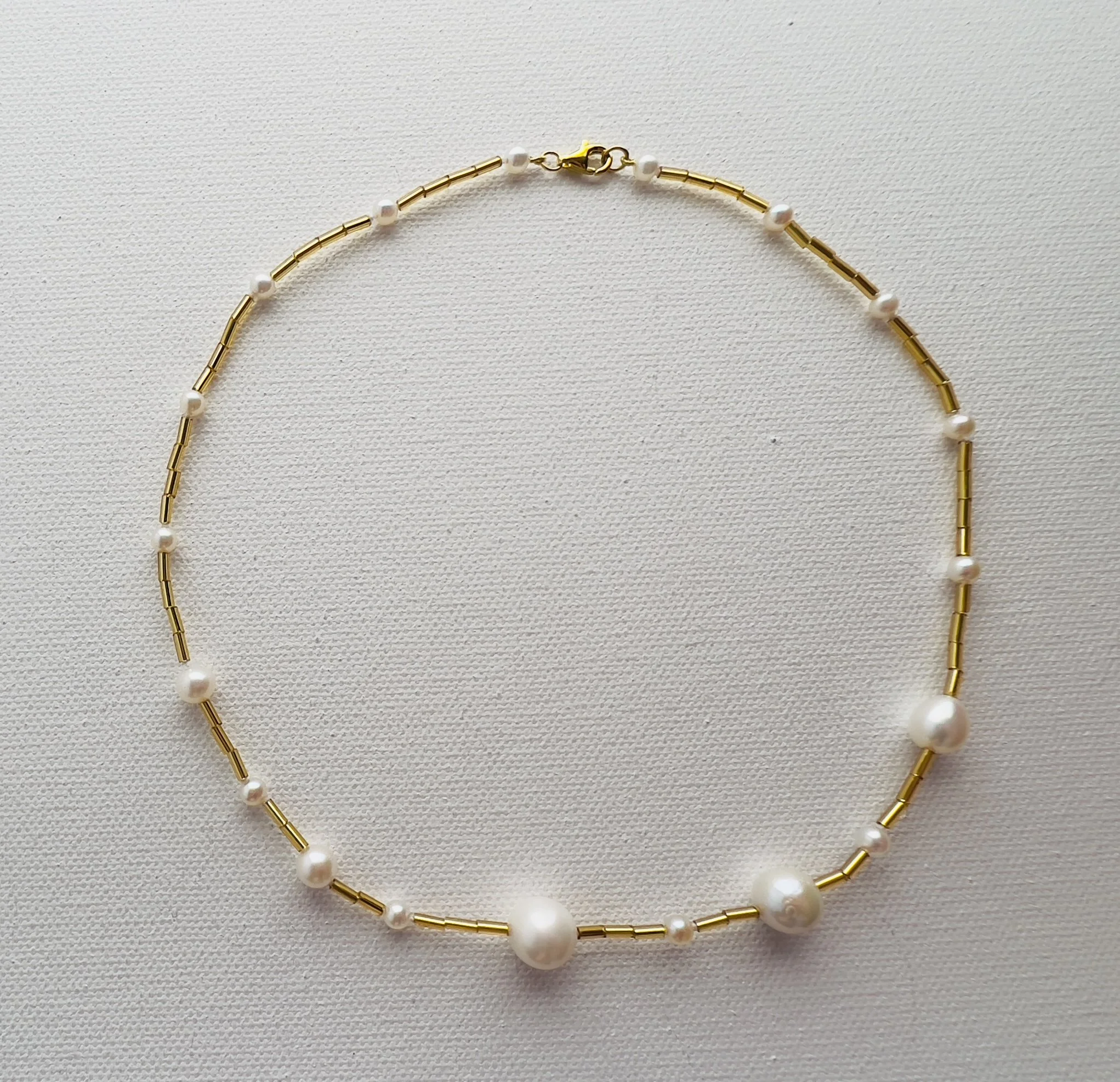 Gold and pearl beaded necklace on a white textured background.