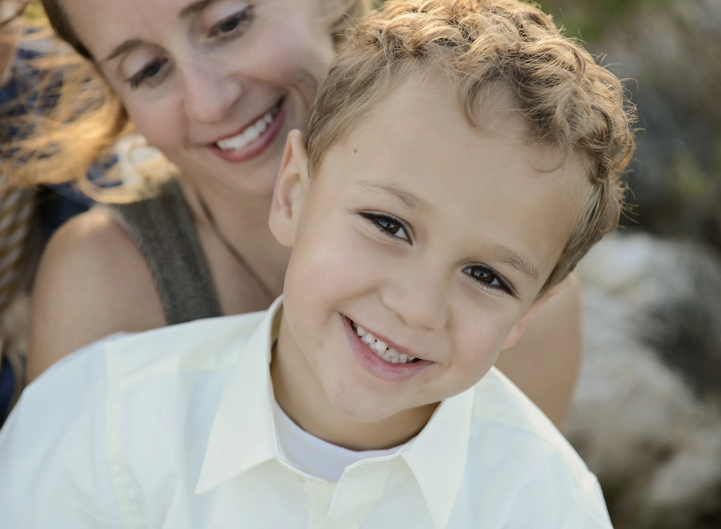 Young boy smiling at camera with a smiling woman behind him