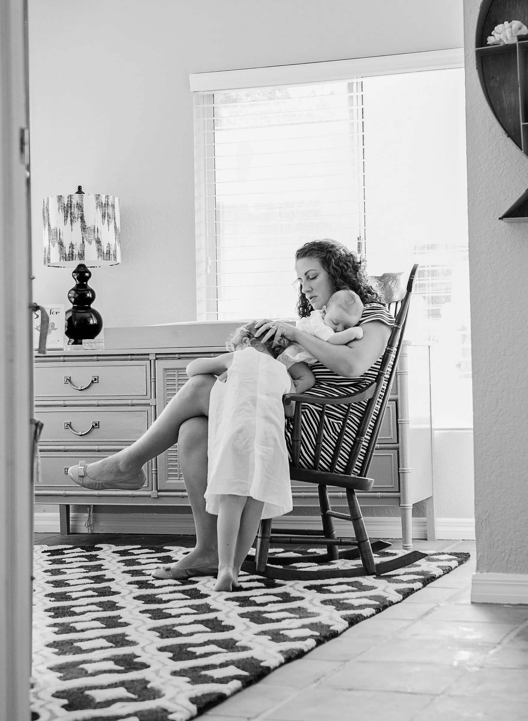 Woman in a rocking chair holding a newborn baby and comforting a toddler