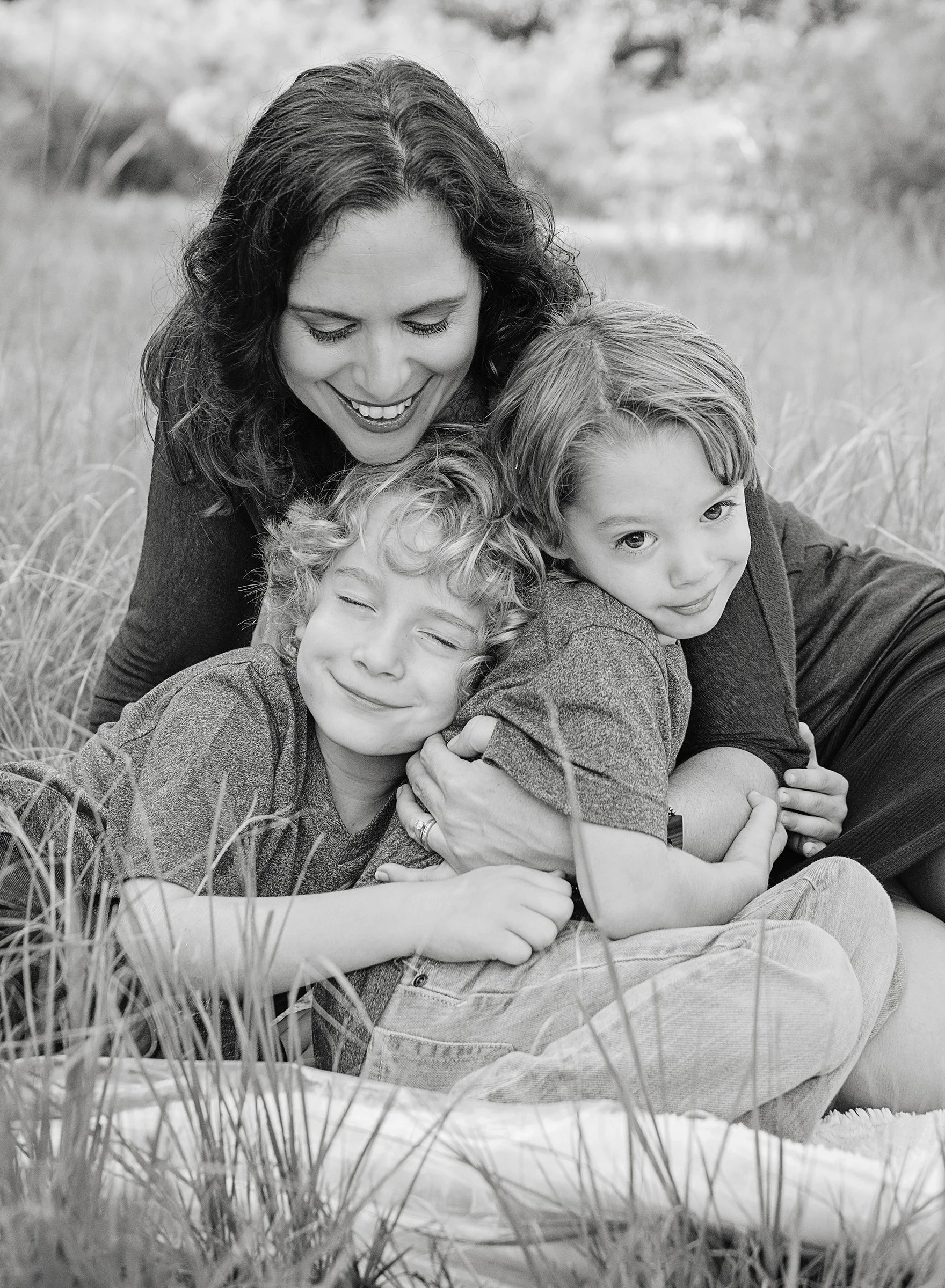 Woman sitting the ground hugging two boys in a field in Odessa