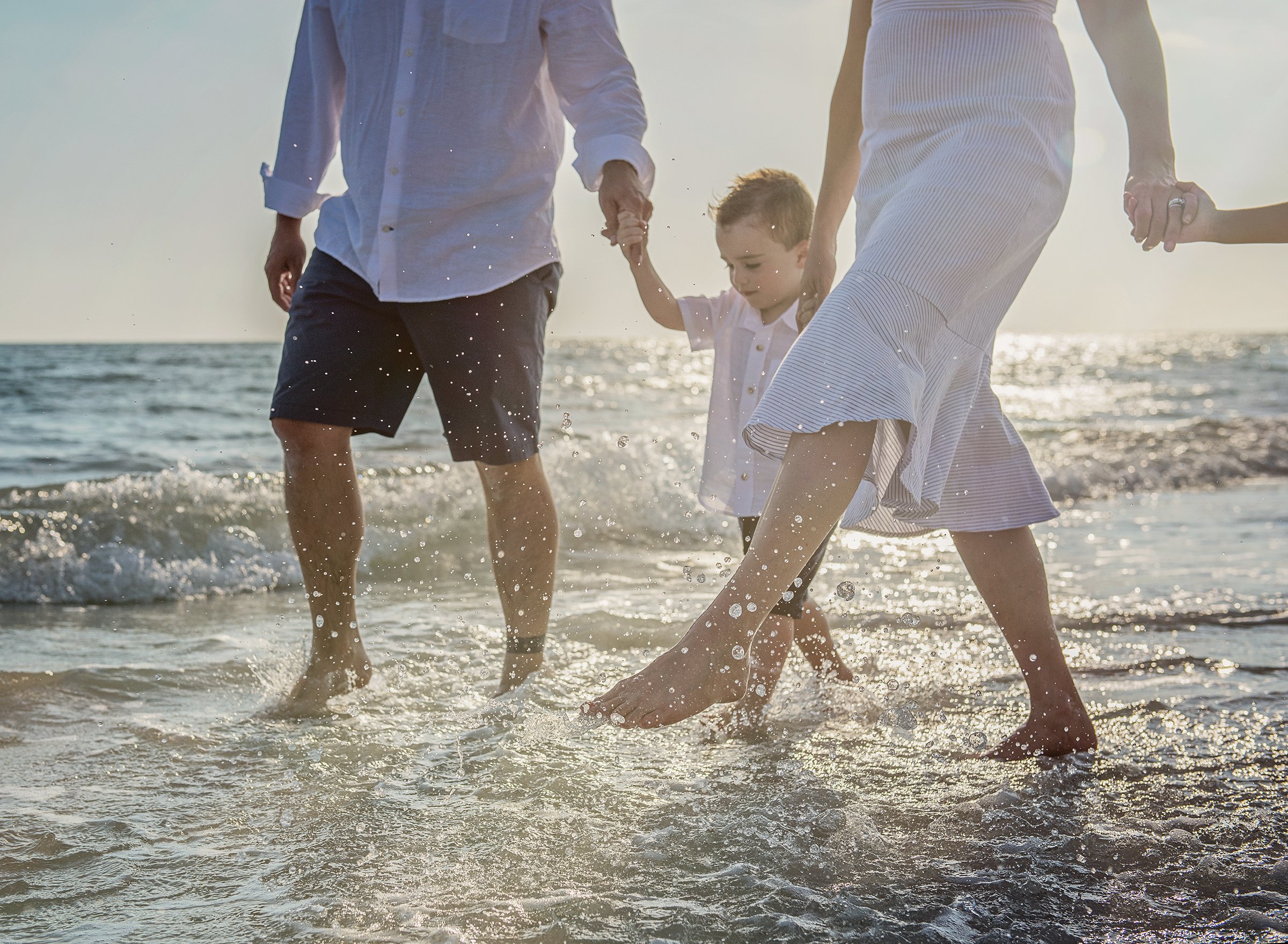 Young boy holding parent's hands walking in the water at Madeira Beach