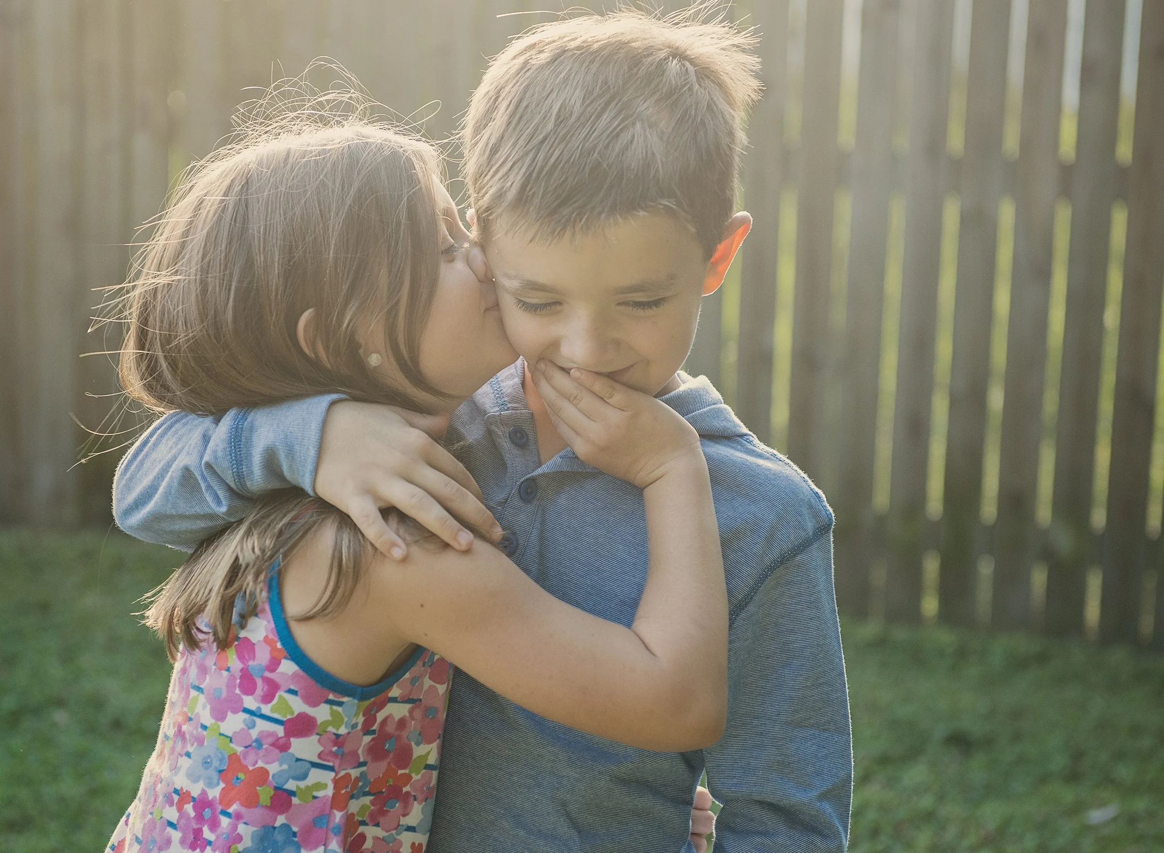 Young girl whispering in a young boy's ear and covering his mouth with her hand