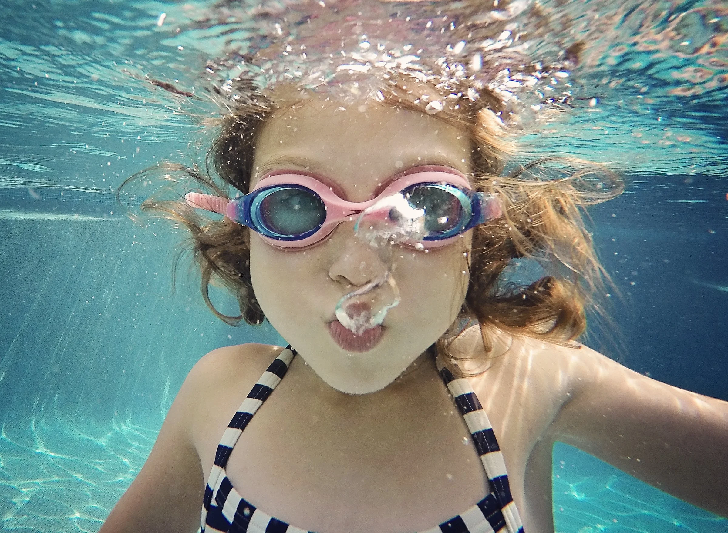Young girl wearing goggles and blowing bubbles under water