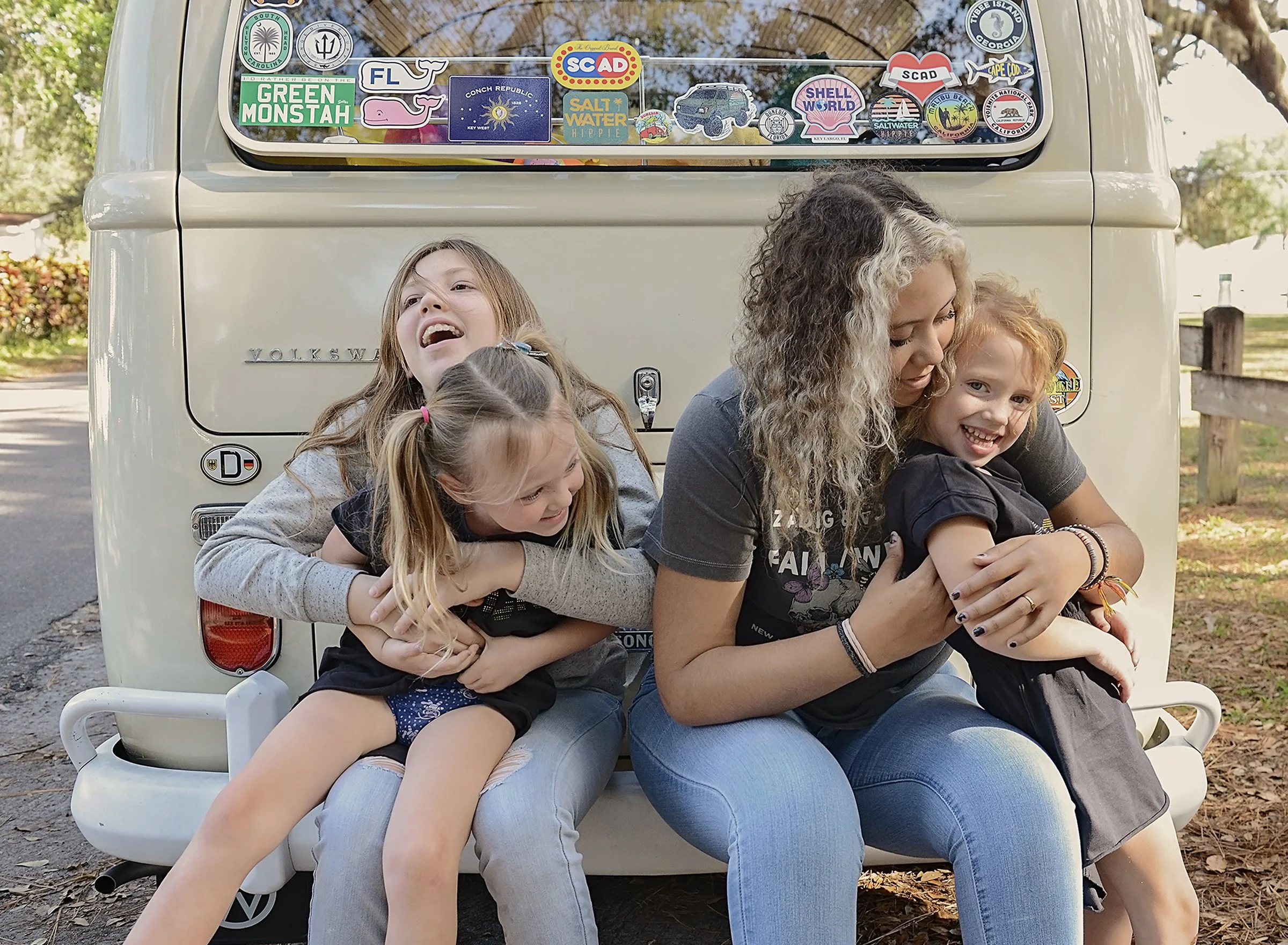 Four girls sitting on the back of a VW bus, hugging and laughing