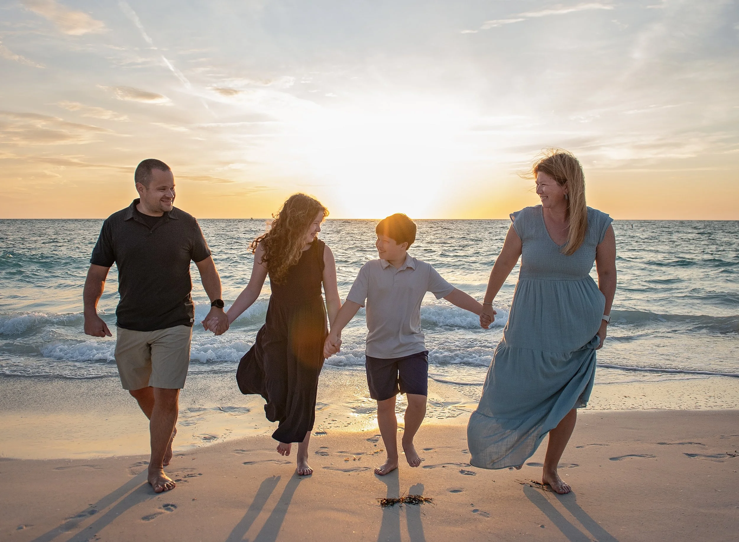 Family of four on the beach with the sunset behind them