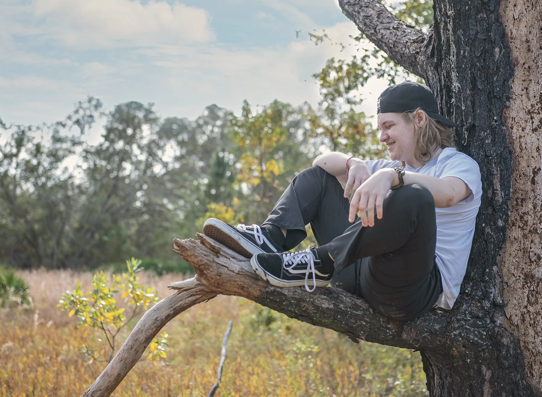 Teen boy sitting in an old tree in a grassy field in Odessa