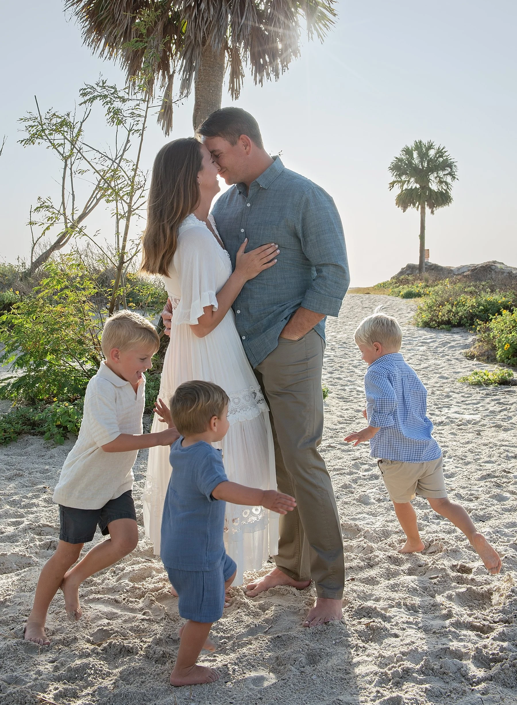 Man and woman hugging on a beach with three young boys running around them