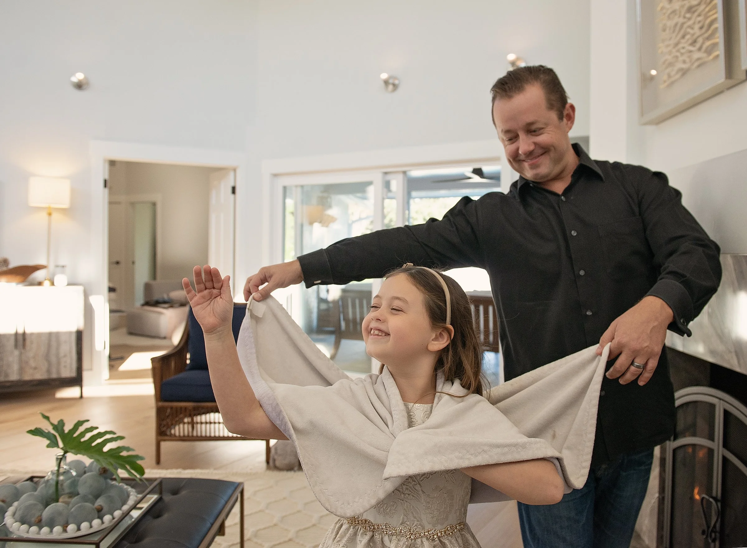 Man walking behind young girl, holding her cape in a photo session at home