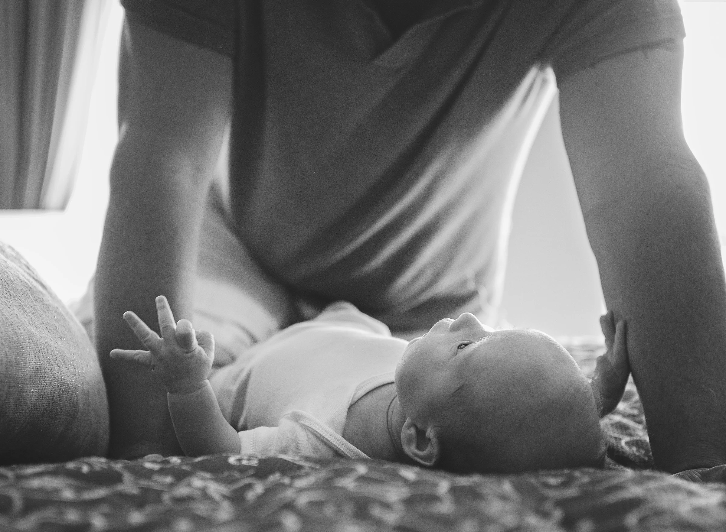 Newborn baby laying on a bed looking up at a man
