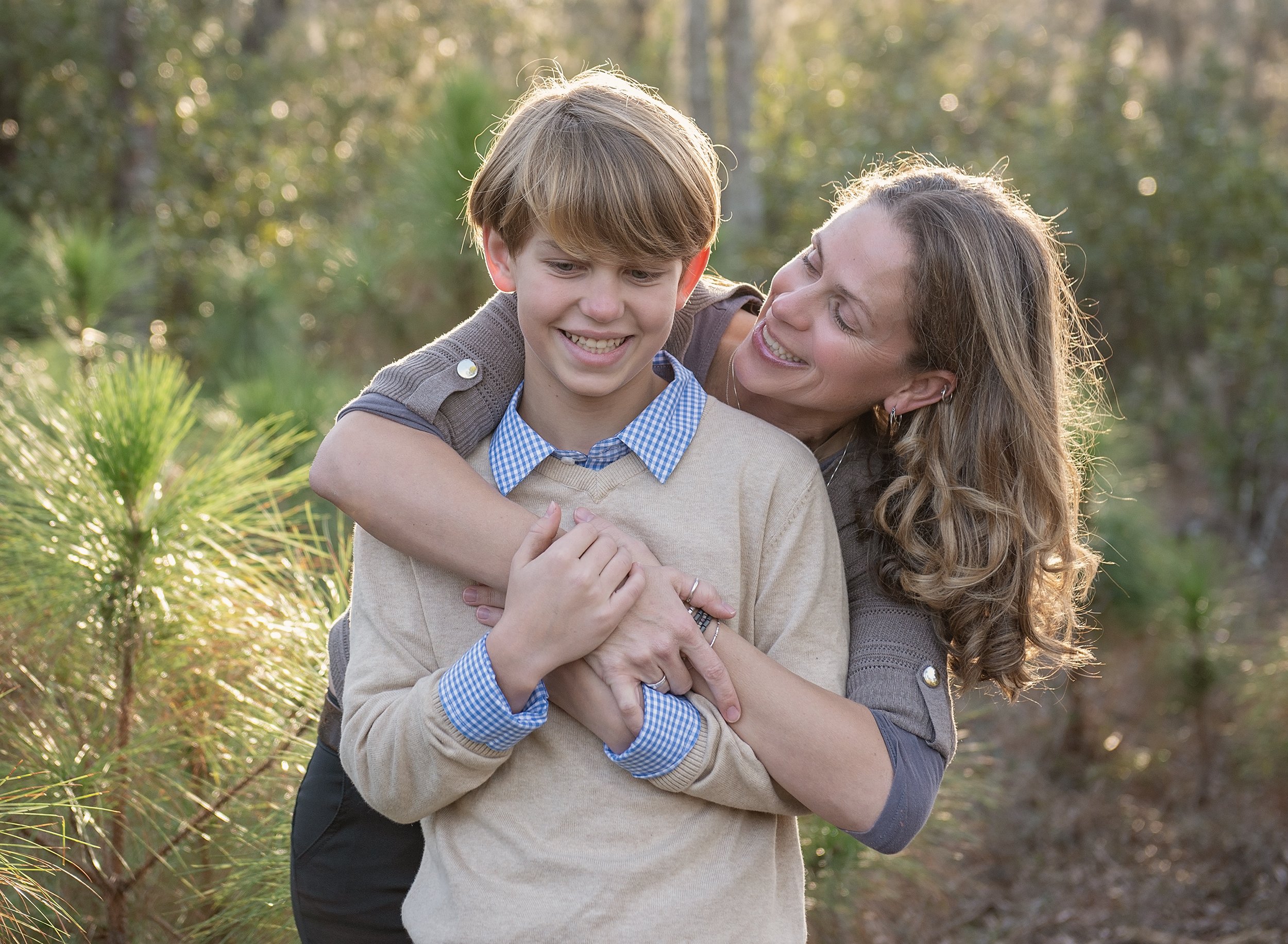 Smiling woman hugging boy from behind at sunset 