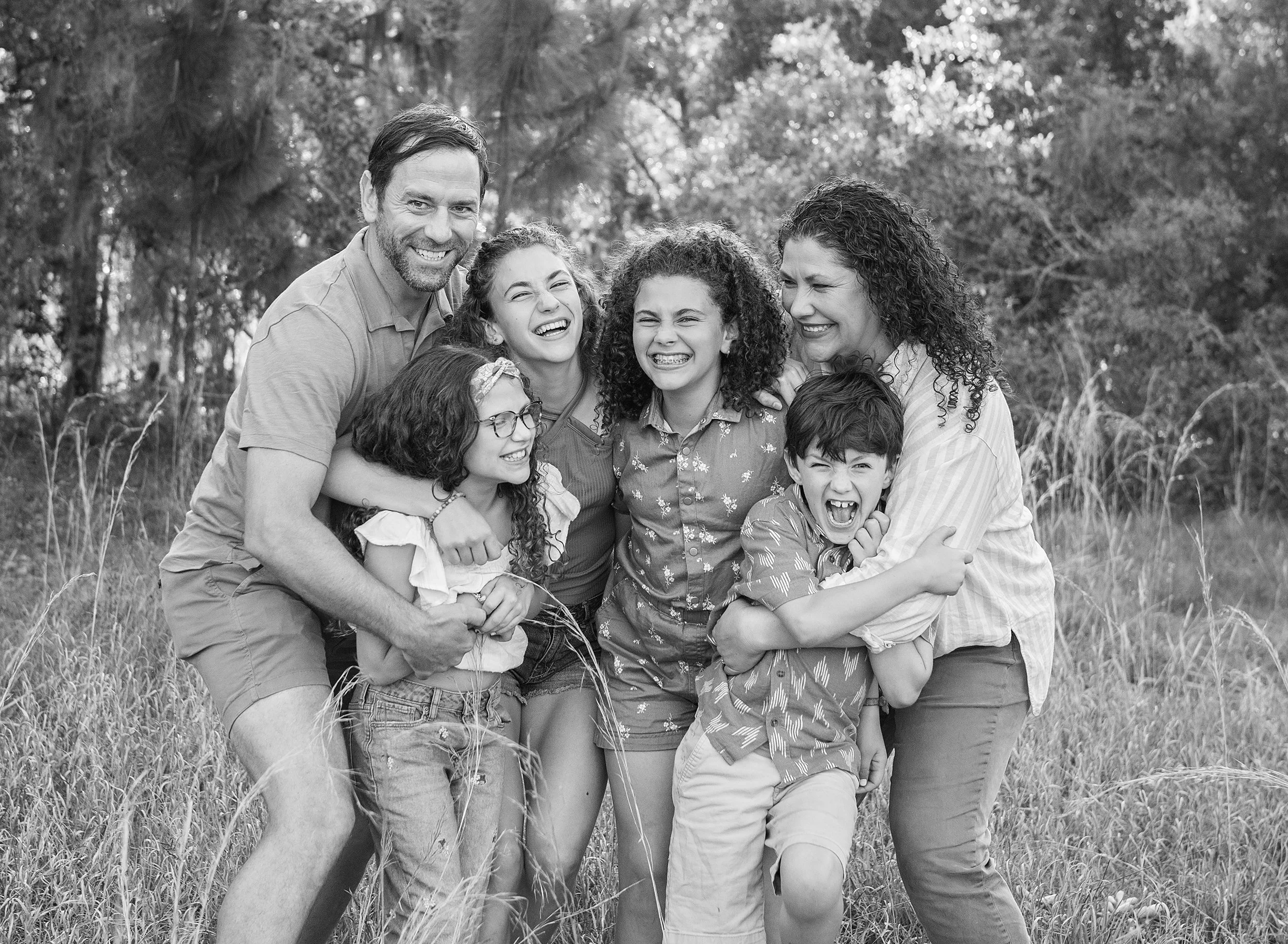 Family of six hugging in a field with tall grass around them