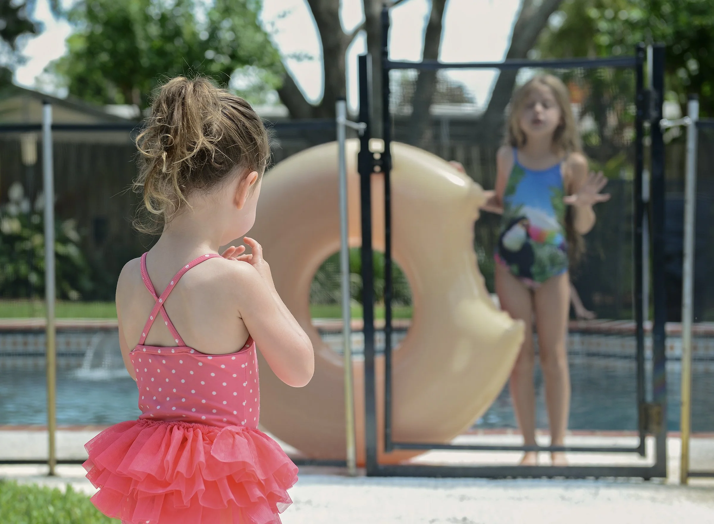 Young girl in a bathing suit staring at an older girl by a pool