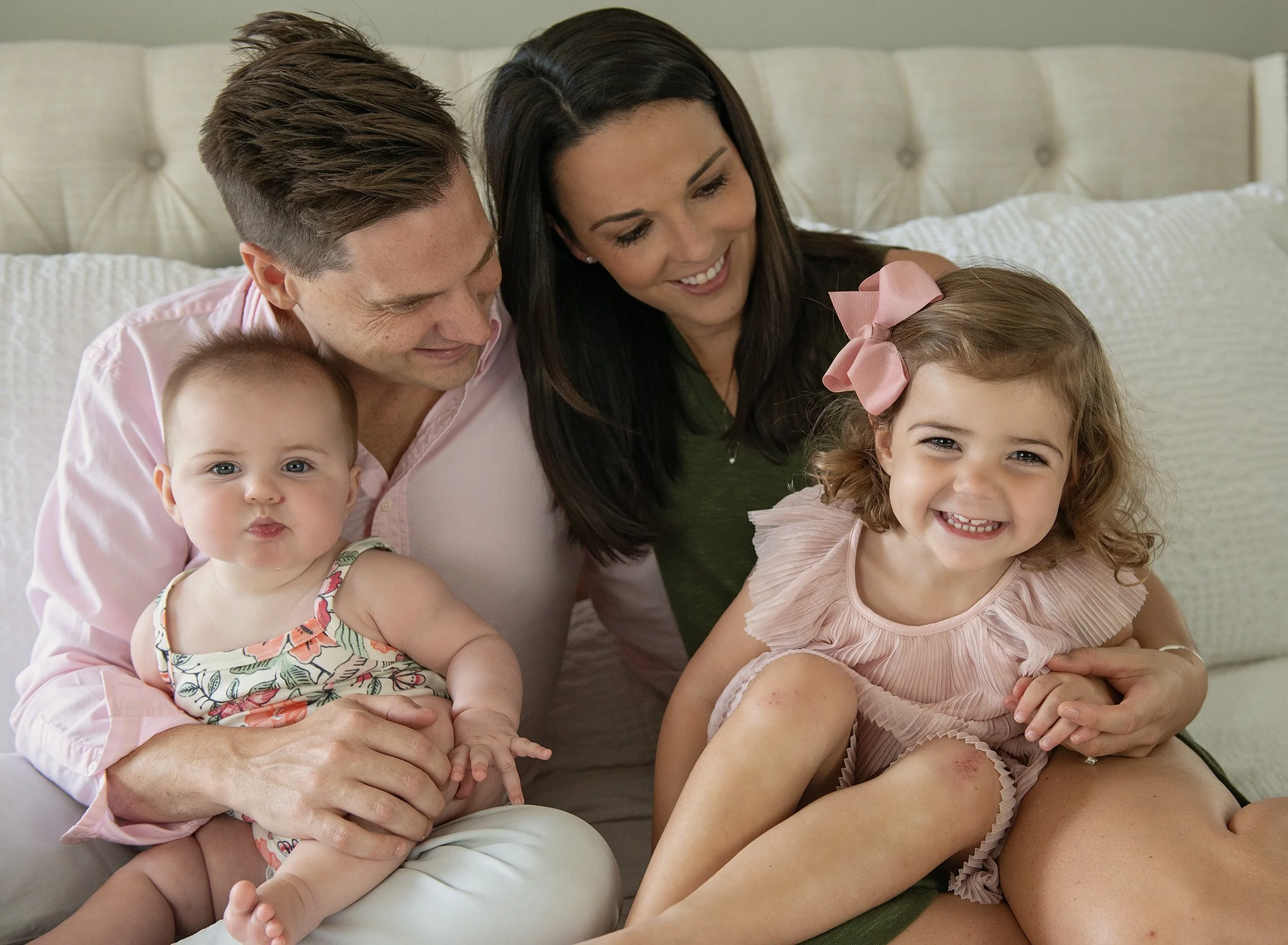 Man and woman with toddler and infant sitting on a bed snuggling