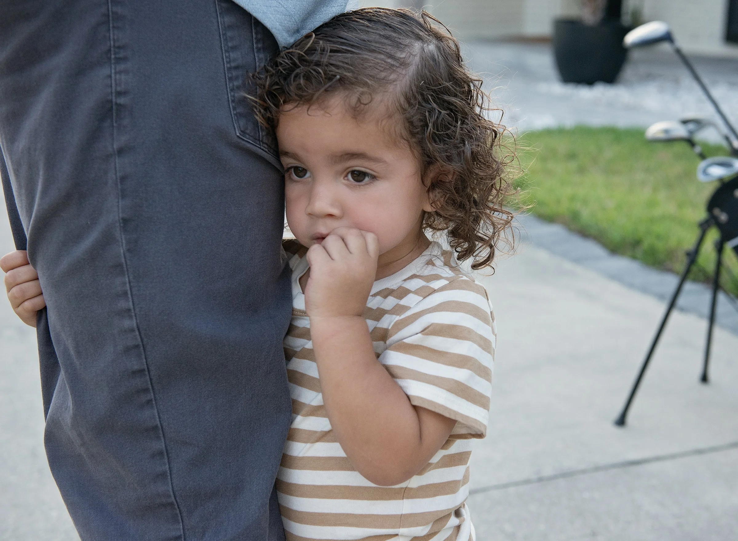 Toddler hugging man's leg with golf clubs in background