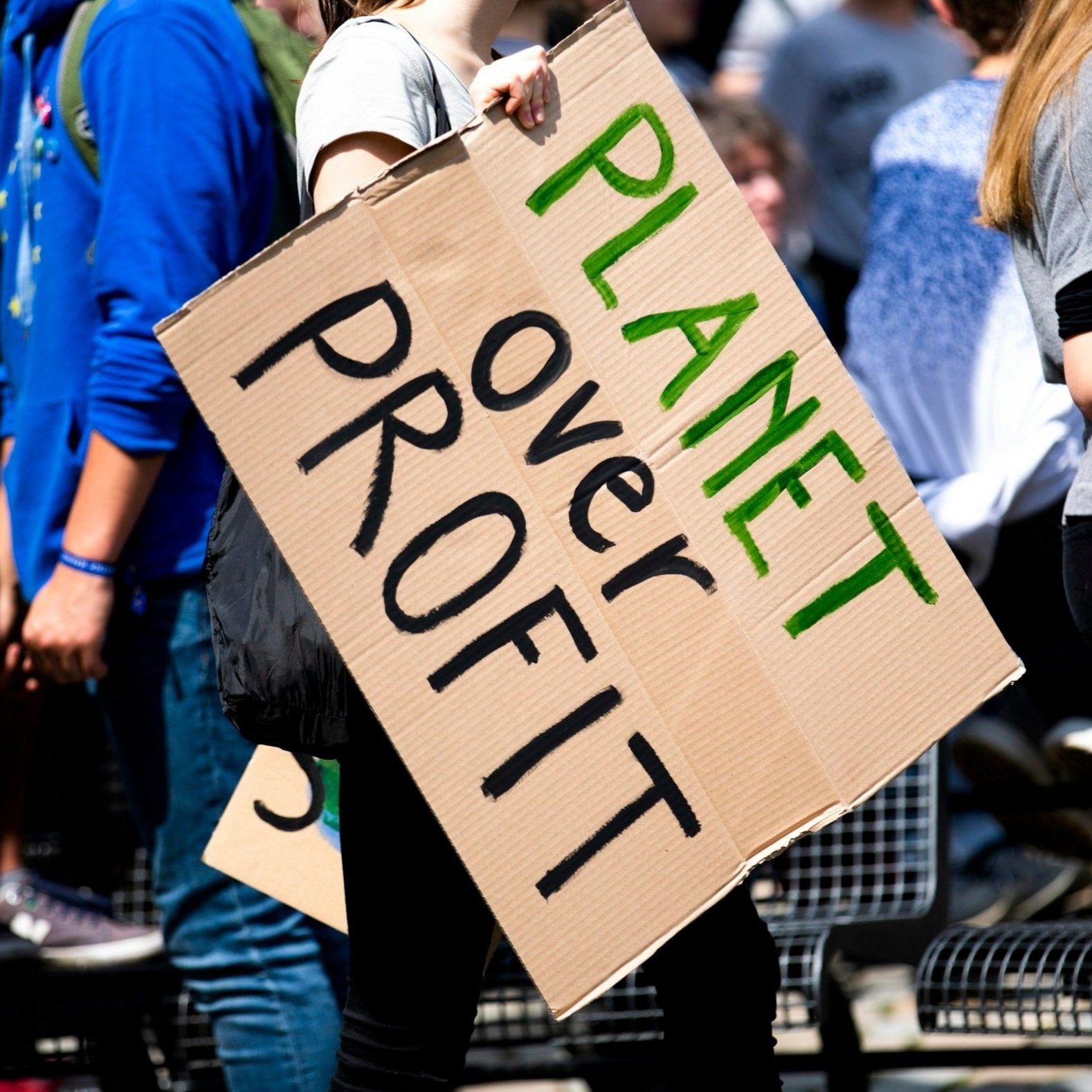 A protester holding a cardboard sign with the words 'PLANET OVER PROFIT'.