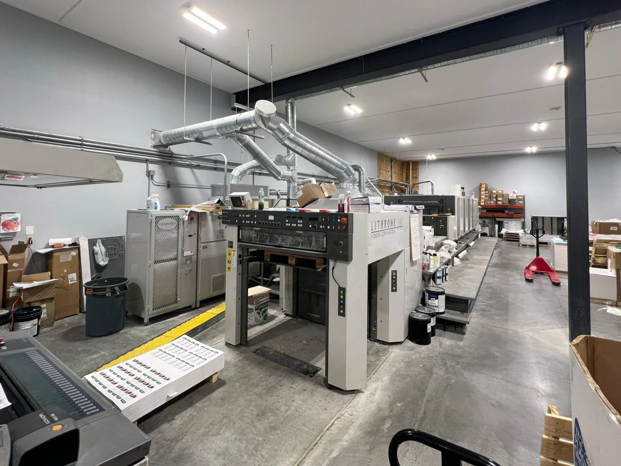 Industrial printing equipment in a warehouse with stacked boxes and supplies.