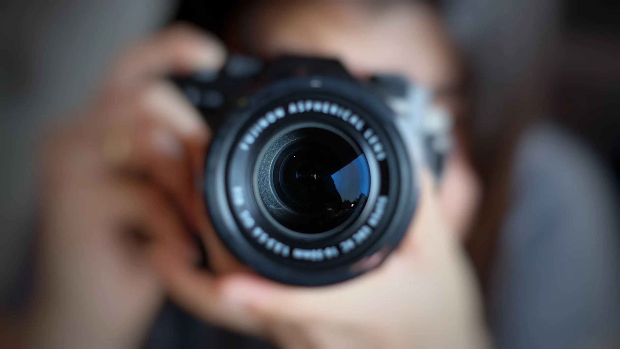 Close-up of a camera lens with a person holding the camera and looking through the viewfinder