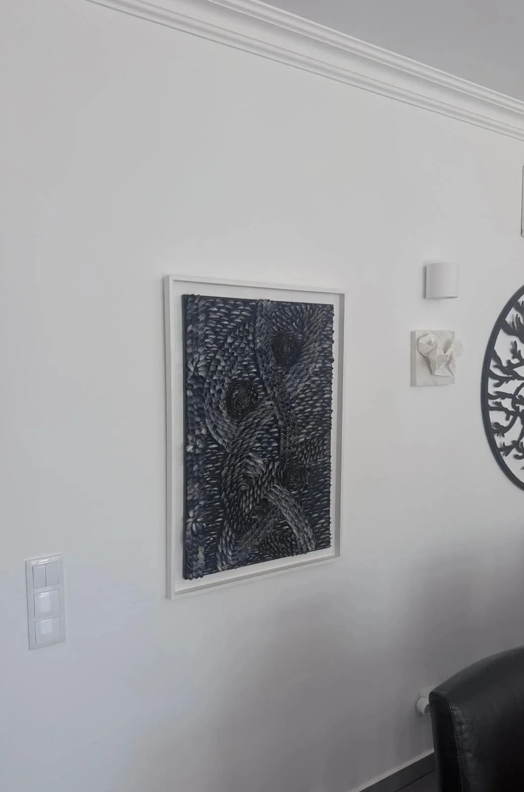 Abstract black and white artwork, made of mussel shells  with swirling patterns on a white wall.