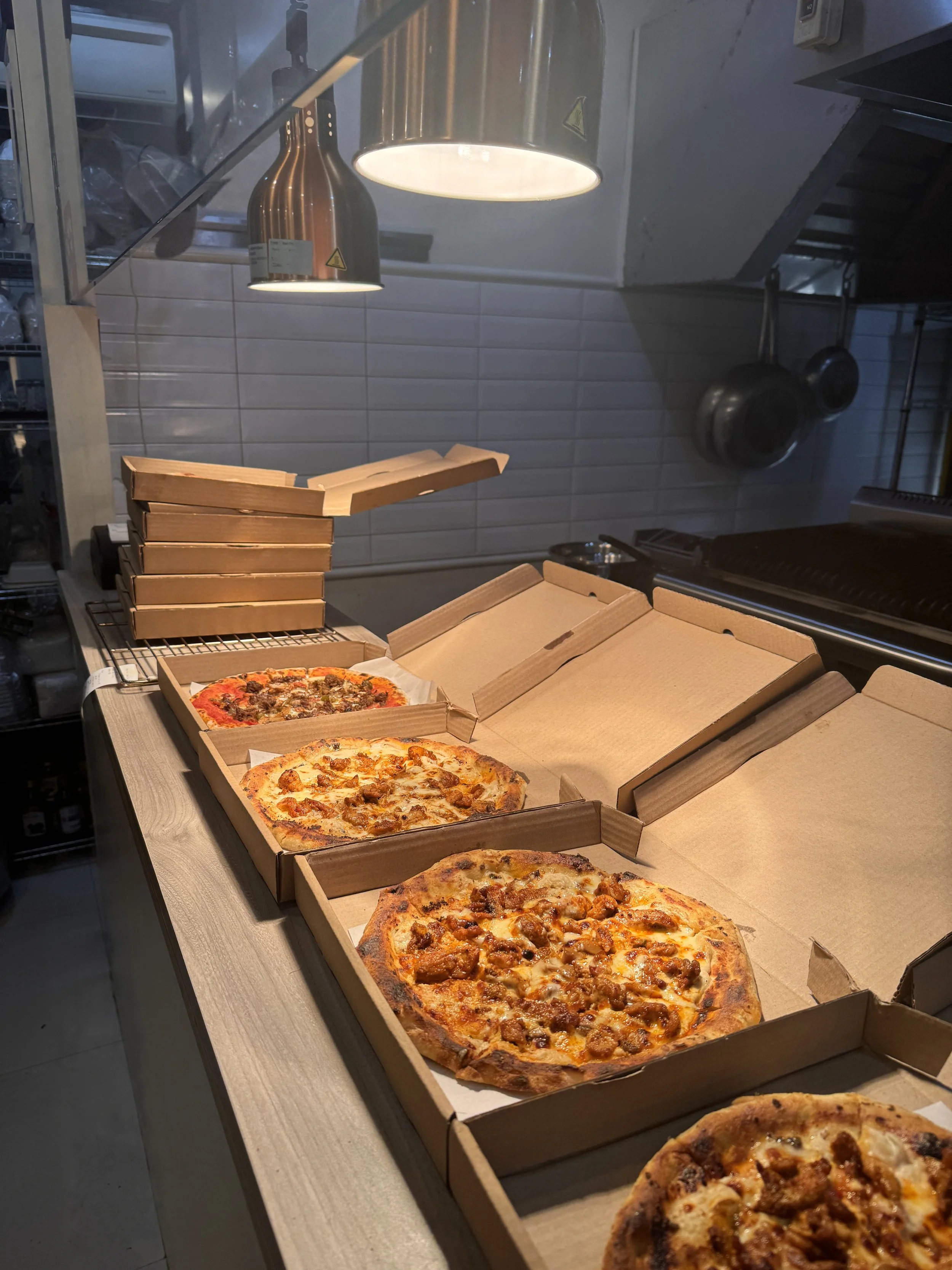 Three opened pizza boxes with pepperoni and sausage pizzas on a wooden countertop in a kitchen.