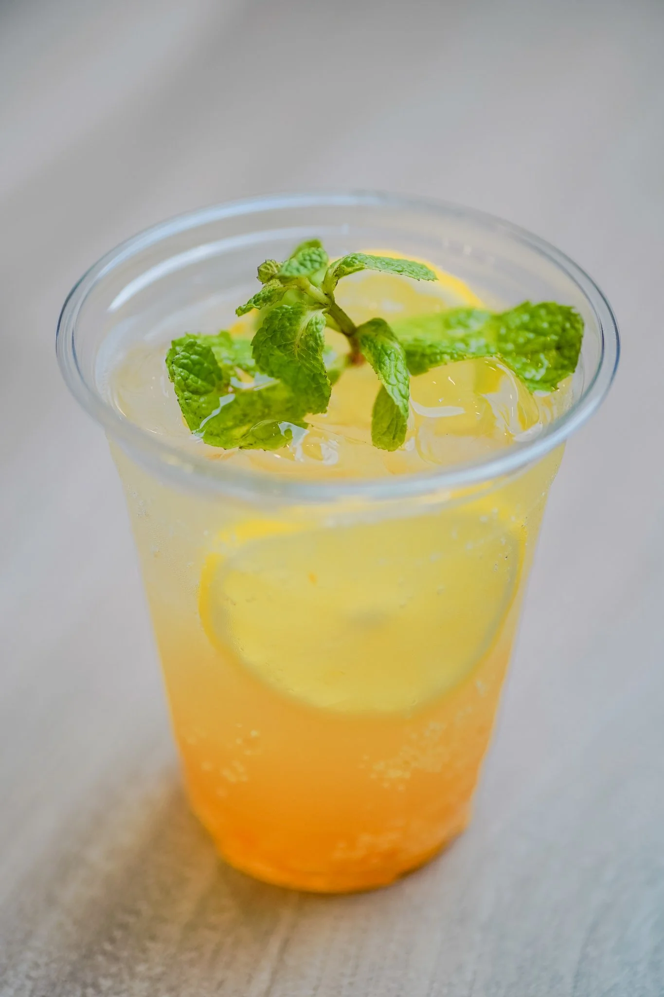 A glass of citrus-colored beverage garnished with fresh mint leaves and a lemon slice.