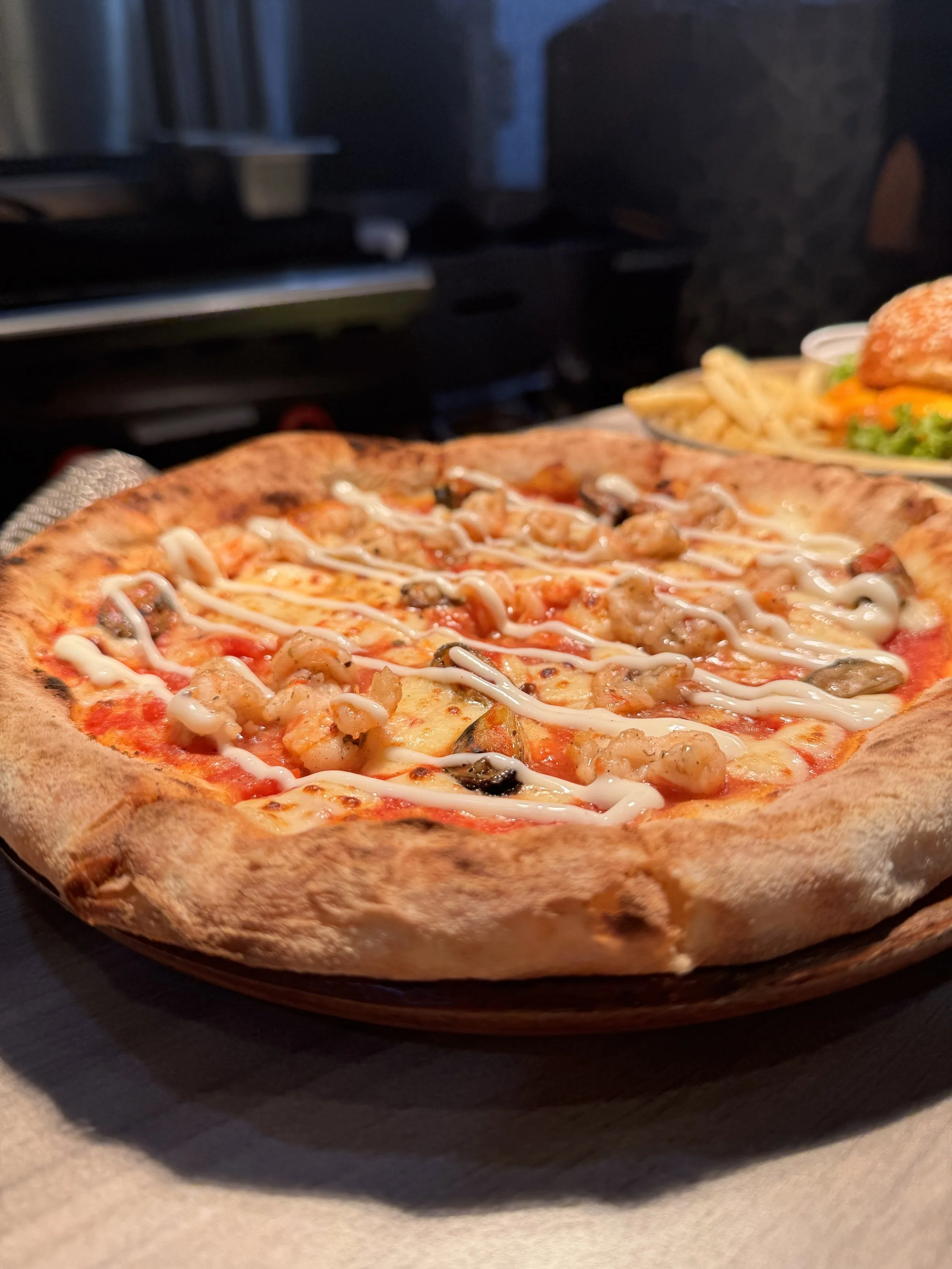 Close-up of a pizza with toppings including shrimp, black olives, and drizzled white sauce.