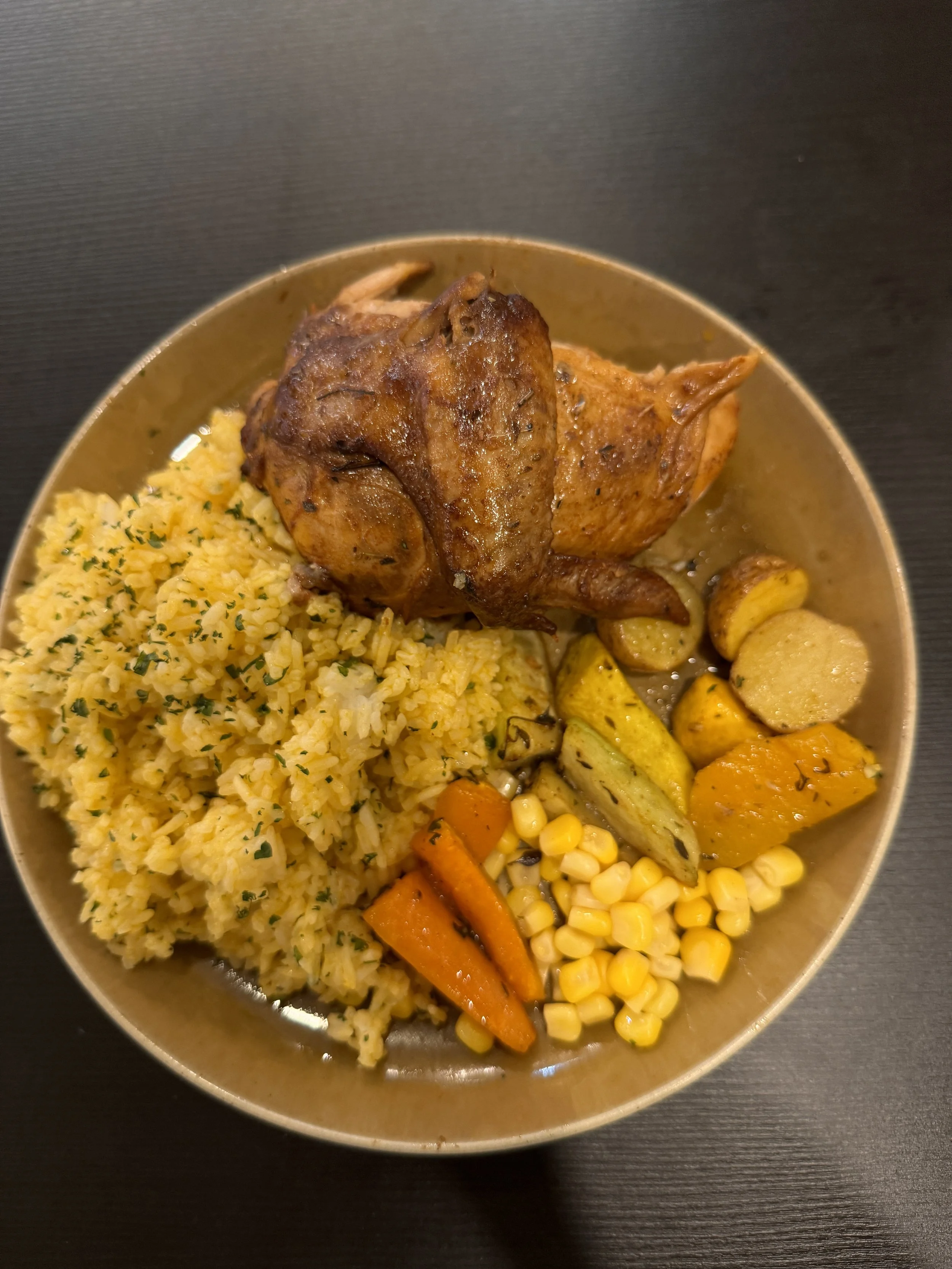 A plate of Indian cuisine including yellow rice, roasted chicken, roasted potatoes, carrots, corn, and zucchini.