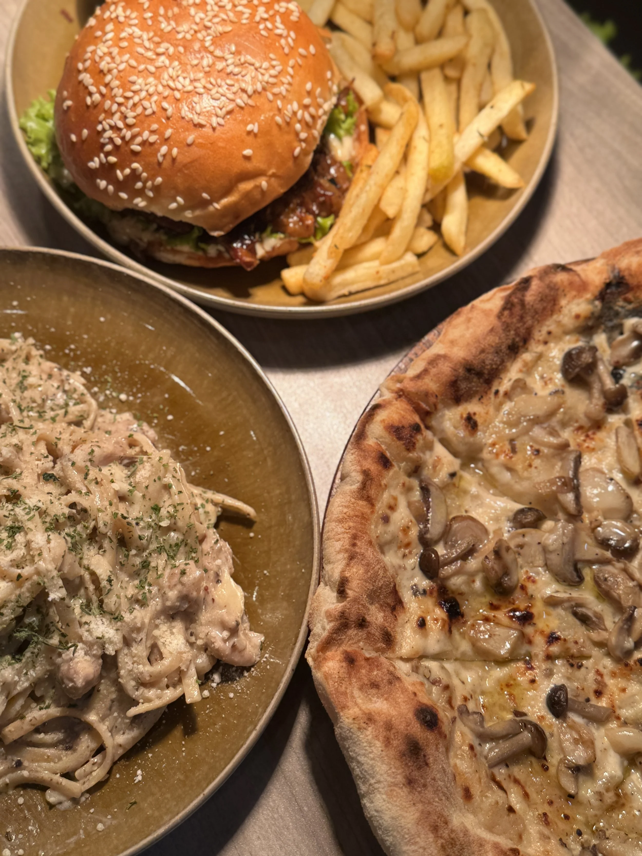 A plate with a cheeseburger and French fries, a bowl of creamy mushroom pasta, and a pizza with mushroom topping.