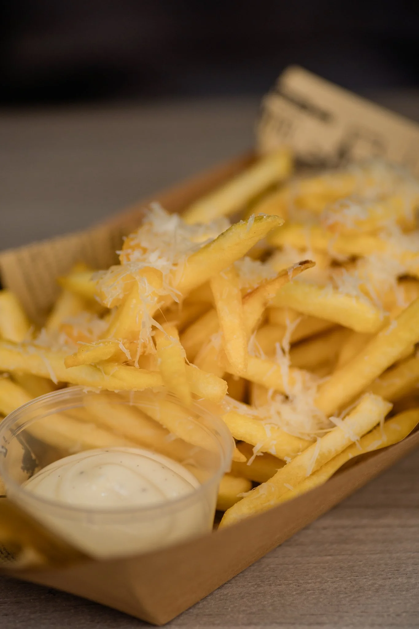 A tray of French fries topped with shredded cheese and a small cup of creamy dipping sauce.