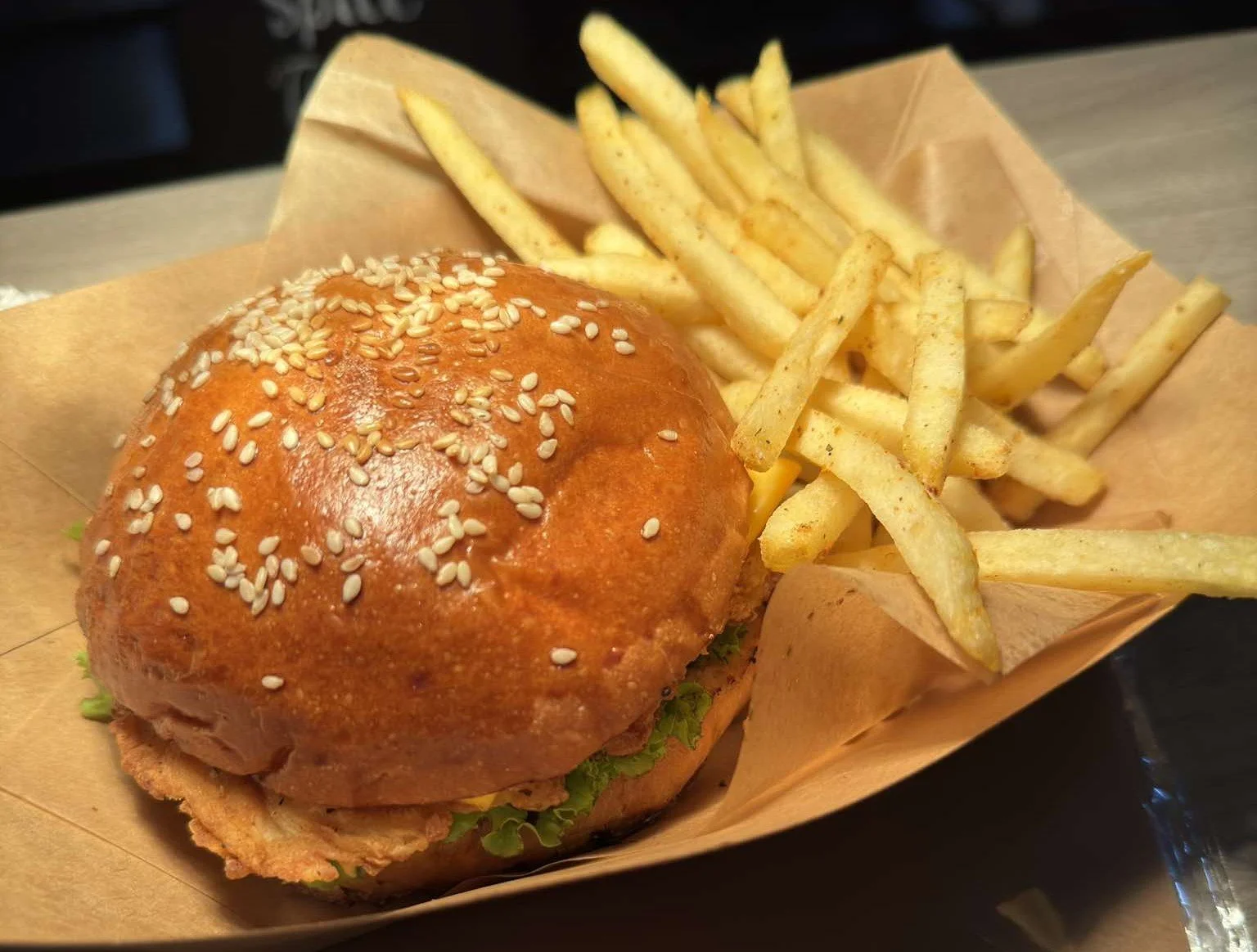 Fried chicken sandwich with lettuce and mayonnaise served with seasoned French fries on brown paper in a basket.