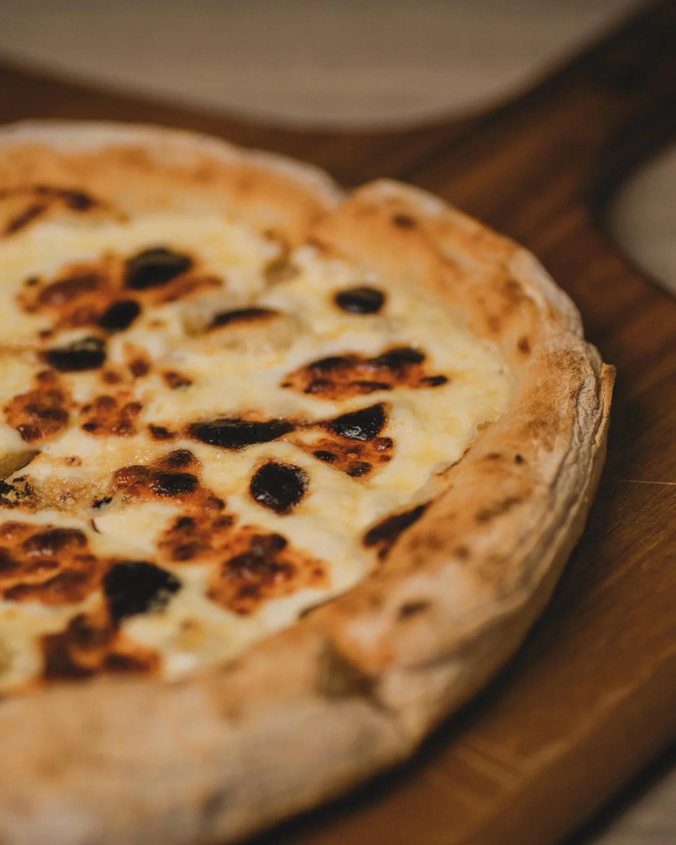 Close-up of a freshly baked pizza with cheese and black olives on a wooden board.
