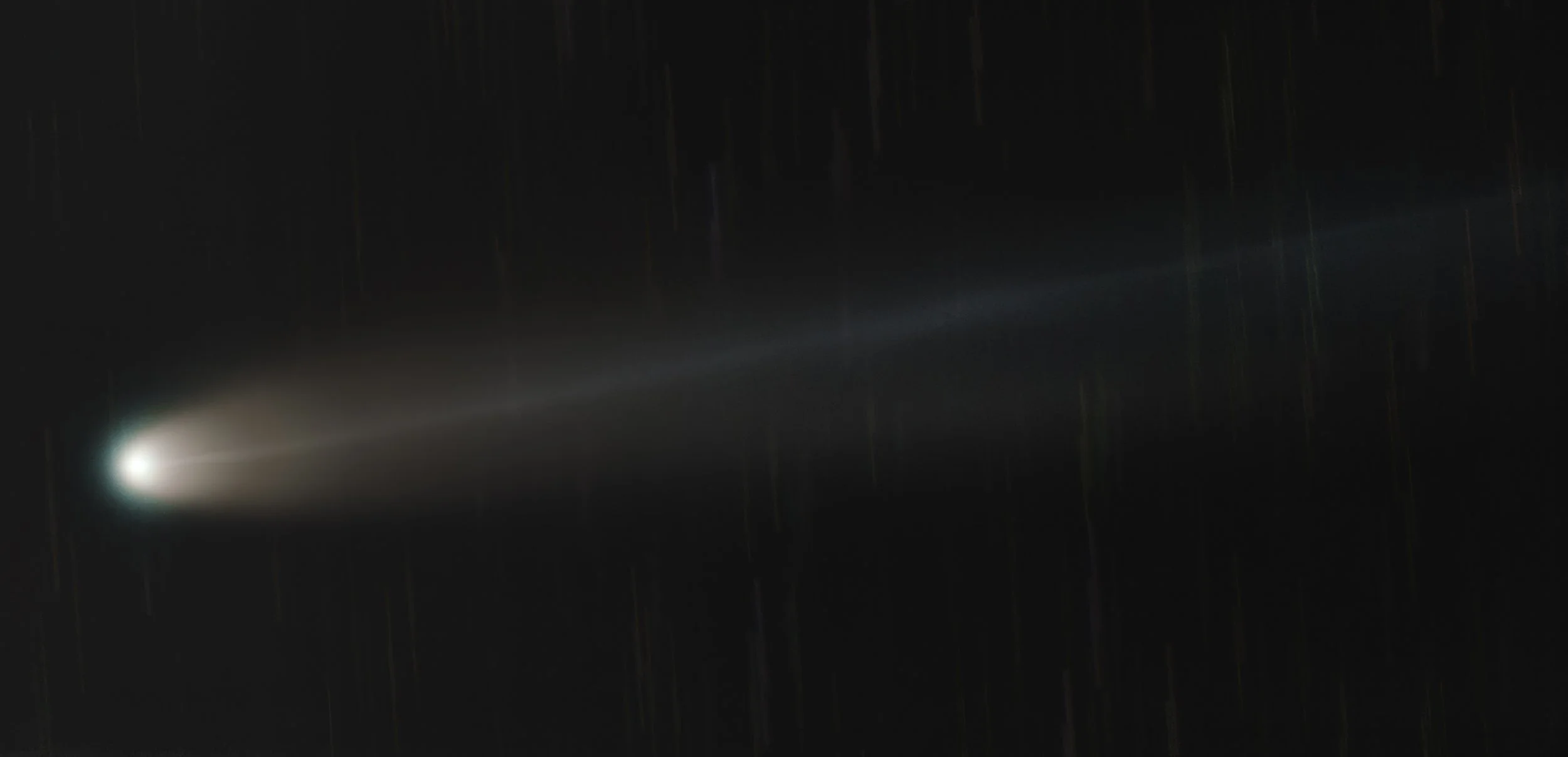 A bright comet with a glowing nucleus and long tail streaking across a dark night sky.