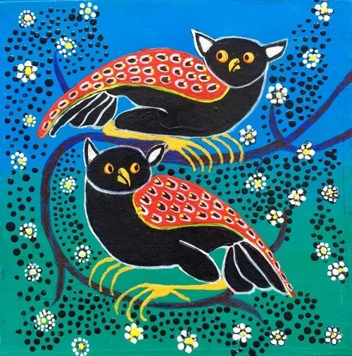 Zwei schwarze Katzen mit bunten, fischartigen Flügeln sitzen auf Zweigen, umgeben von kleinen weißen Blümchen und blauen Mustern auf einem blauen Hintergrund.