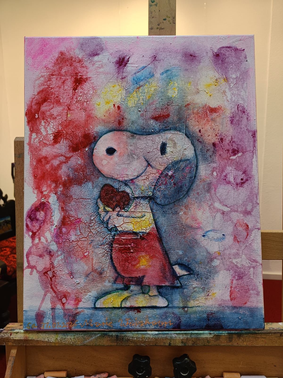 A bunte abstrakte Malerei mit einer Zeichnung von Peanuts' Charakter Charlie Brown, der ein Herz hält, vor einem farbenfrohen Hintergrund mit Rissen und Spritzern in Rot, Blau, Gelb und Lila.