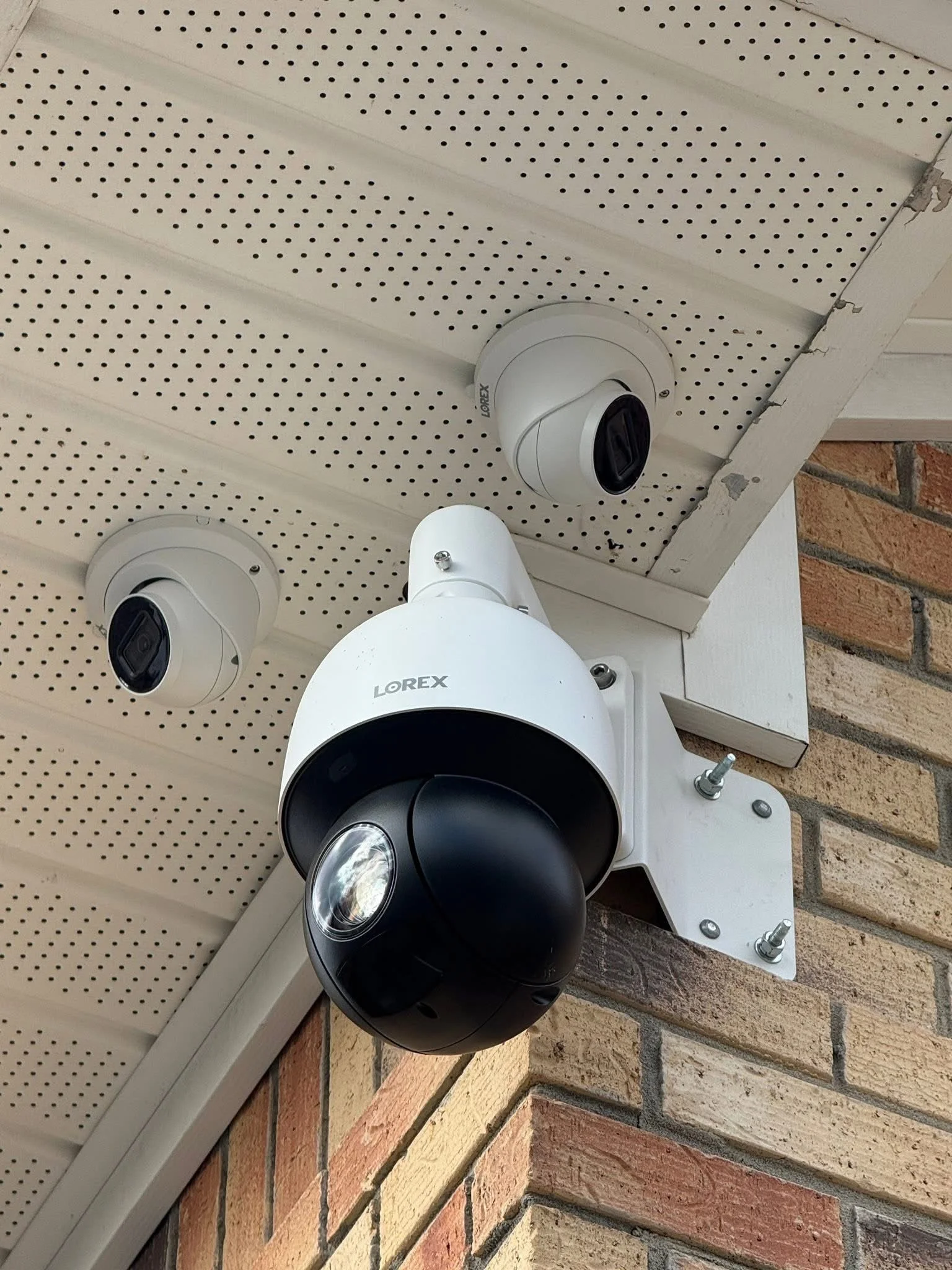 A security camera mounted on a brick wall under a soffit with additional cameras installed nearby.