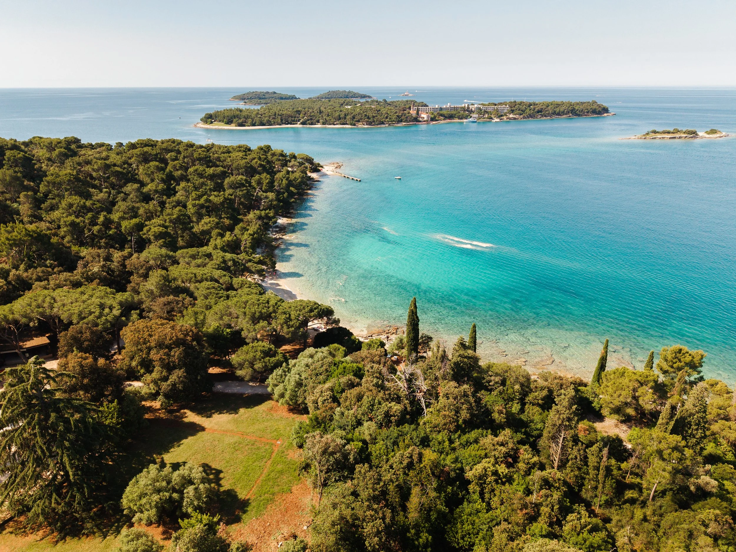 Aerial panoramic photograph of the Red Island / Crveni Otok / Isola Rossa in Rovinj as seen from the Zlatni Rt / Golden Bay beach in Rovinj in Croatia.
