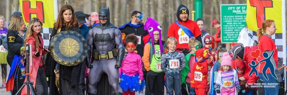 Photo of participants dressed in various superhero costumes smile standing at the starting line of the event ready to take off!